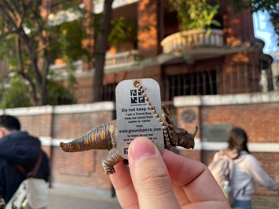 一只手举着恐龙旅行虫，背景是沙面大街68号的红砖楼
