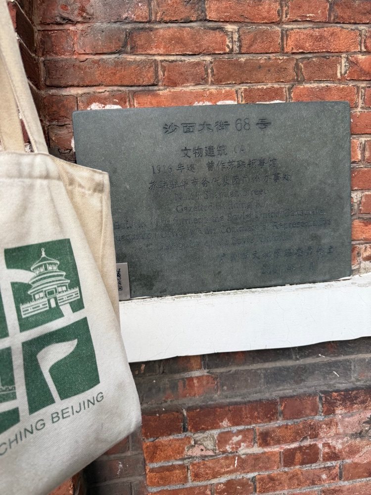 2026年，一只印着 Geocaching 标志的布袋靠在沙面大街68号的铭牌旁